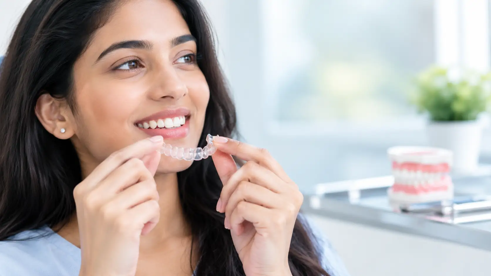Woman-holding-a-clear-dental-aligner-near-her-teeth-in-a-modern-dental-clinic